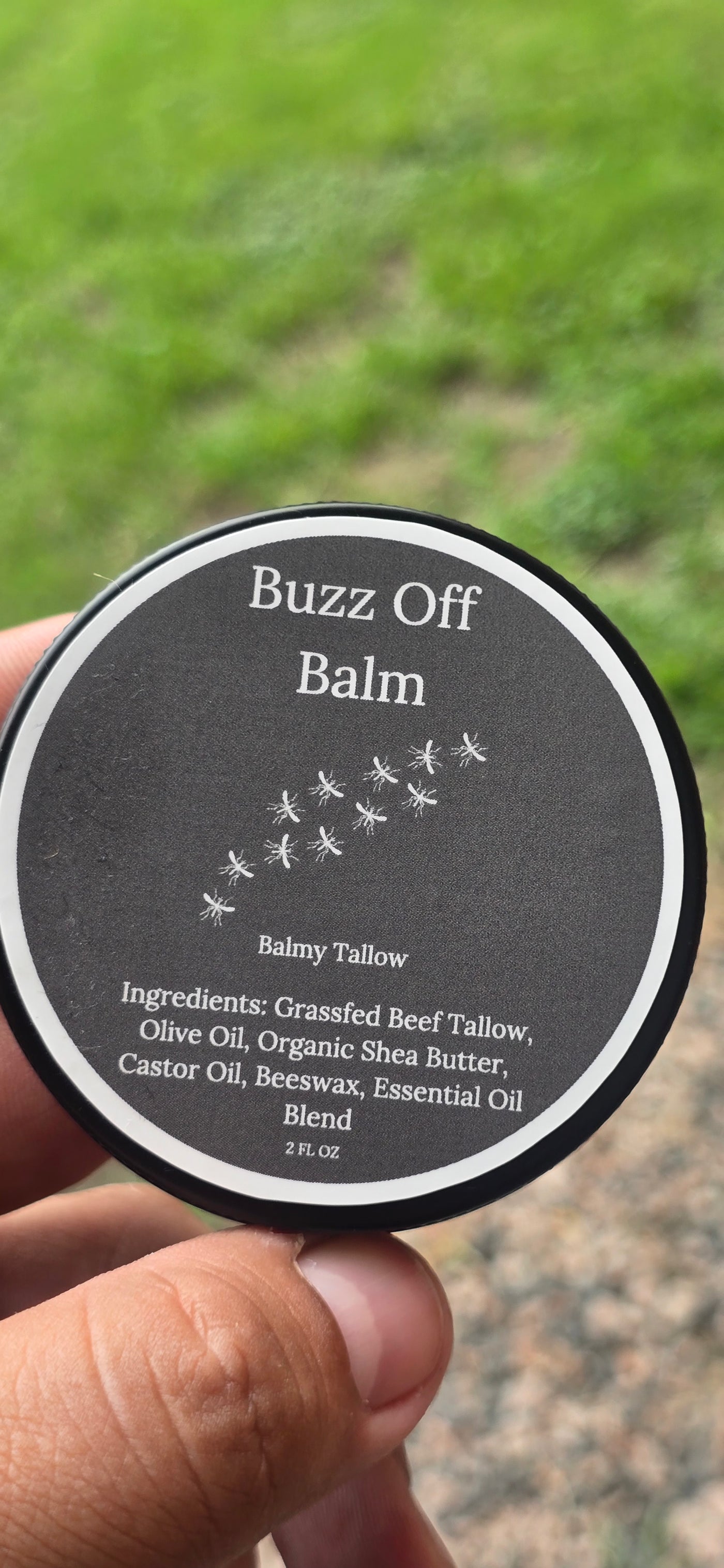 Bug repellant "Buzz Off Balm' held in hand with grassy background