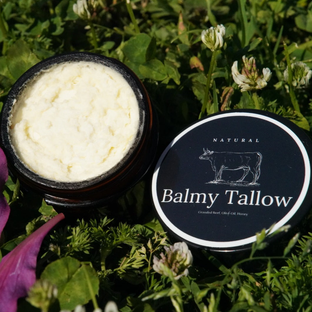 A 2 oz recyclable container of Travel Safe Natural Tallow balm by Balmy Tallow, placed in a natural setting with flowers around it.