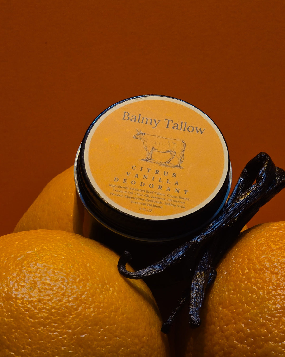 Jar of Balmy Tallow Citrus Vanilla Deodorant with oranges and vanilla beans on an orange background